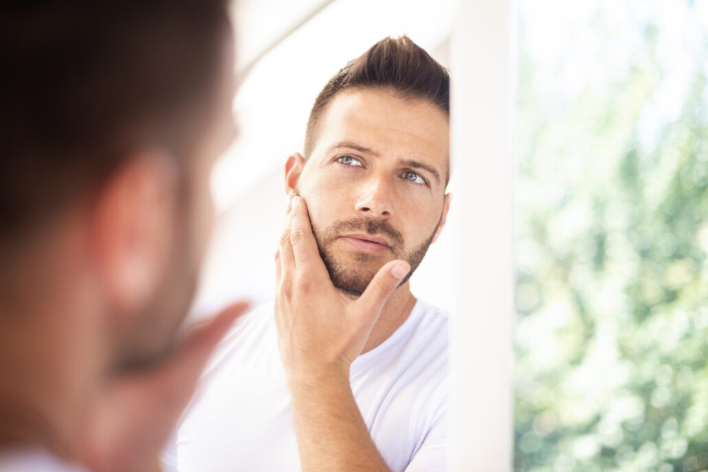 anti aging tips for menClose-up shot of a handsome young man with towel in his neck admiring looking at his face in the bathroom mirror.